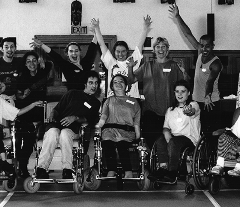 A black and white photograph of a group posing for the camera, there are five people in wheelchairs in the front row and seven others standing behind.
